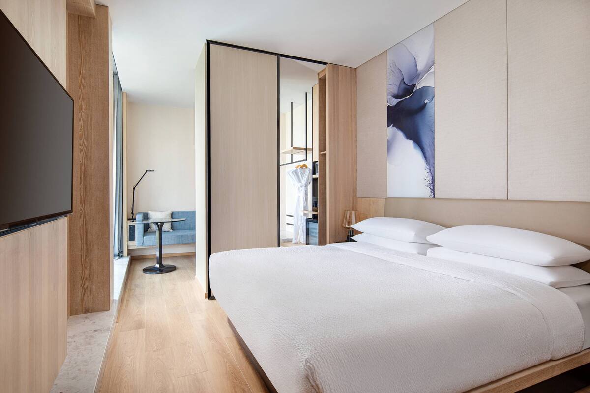 Una habitación de hotel moderna con una cama grande, un televisor de pantalla plana, un sofá y un cuadro en la pared.