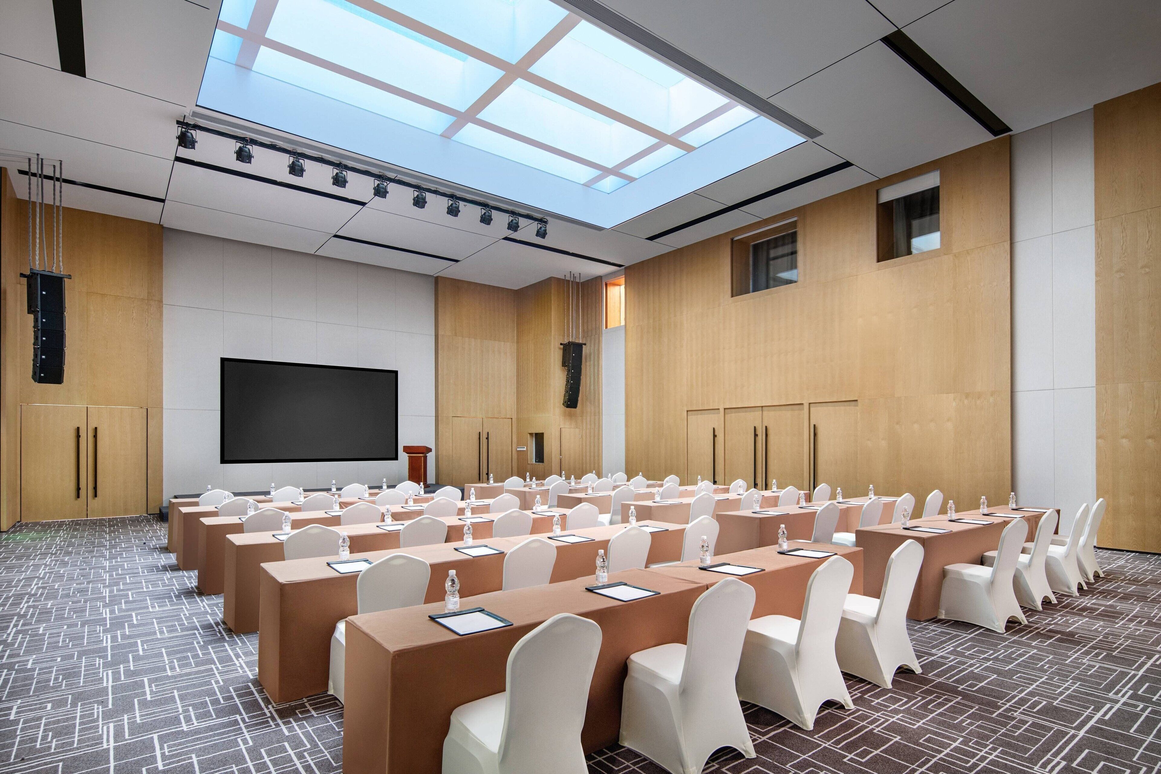 A conference room with a large screen, multiple tables with chairs, and a patterned carpet.