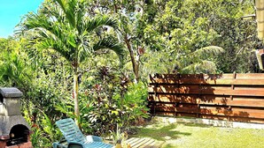 A picnic area with a wooden table and benches, surrounded by lush greenery and a wooden fence. - Bungalow 2 bdrms in quiet flowered park 3 min from beach and 5 min from town (Deshaies)