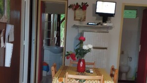 A dining area with a wooden table and chairs, a vase with flowers, and a television on the wall. - Bungalow 2 bdrms in quiet flowered park 3 min from beach and 5 min from town (Deshaies)