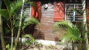 A wooden house with red shutters and a white roof. - Bungalow 2 bdrms in quiet flowered park 3 min from beach and 5 min from town (Deshaies)