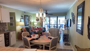 A spacious living room with a dining area, a kitchen, and a balcony with a view. - Escape to Classic Anna Maria Island Charm (Bradenton Beach)