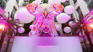 A large, colorful elephant sculpture in a courtyard with white balloons and palm trees.