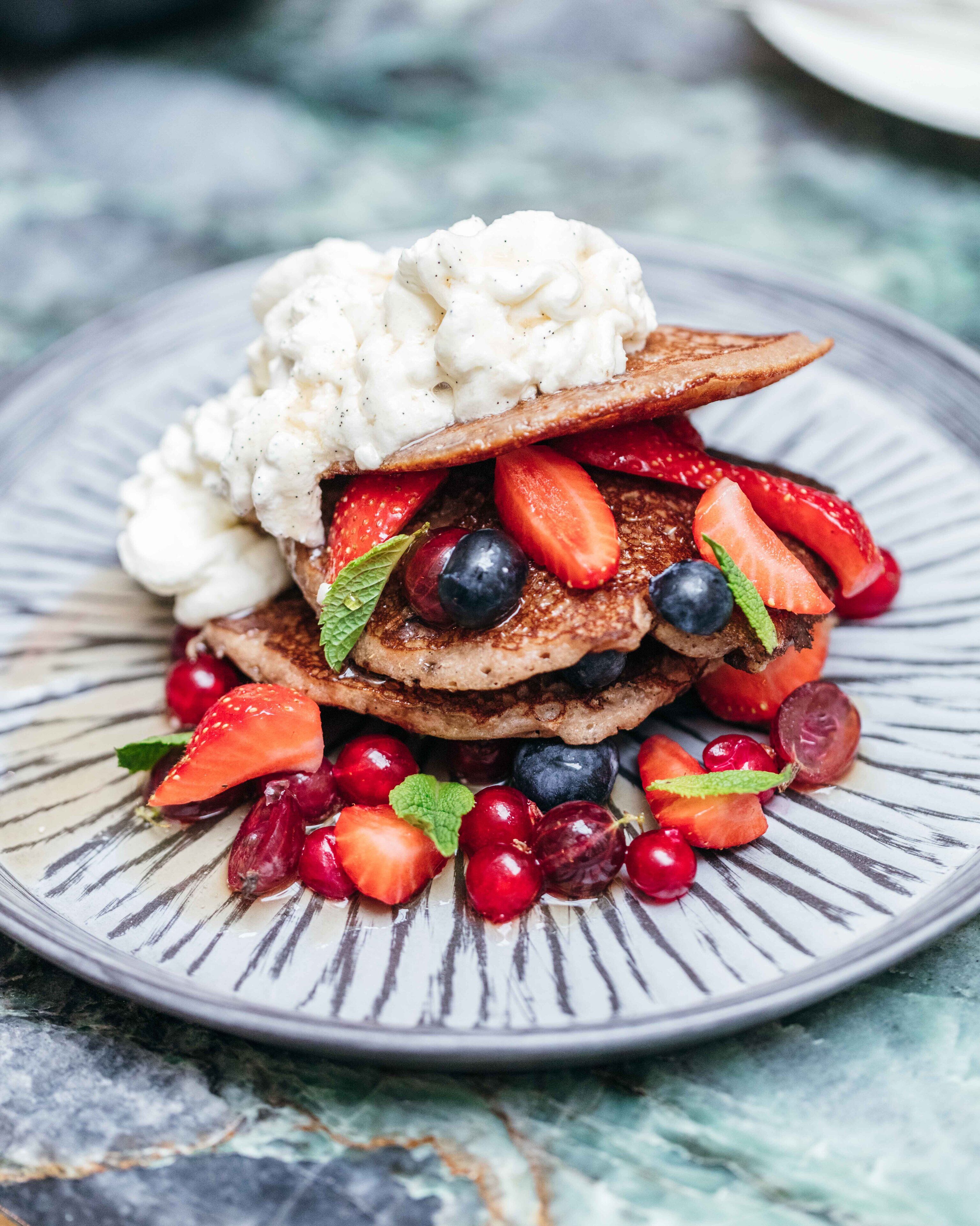 A stack of pancakes with strawberries, blueberries, and a dollop of cream on a plate.