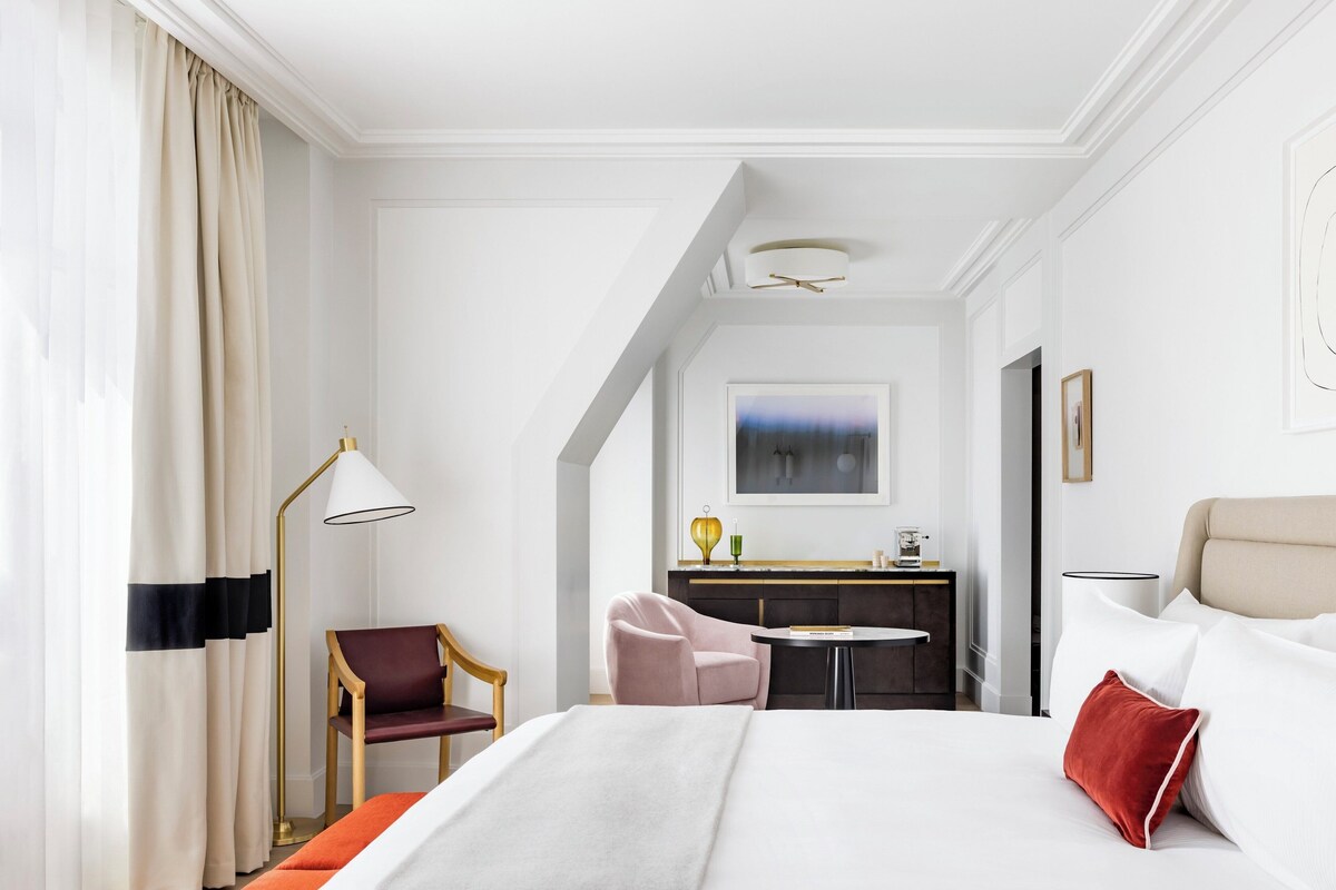 A hotel room with a large bed, a desk, a chair, and a view of the city.