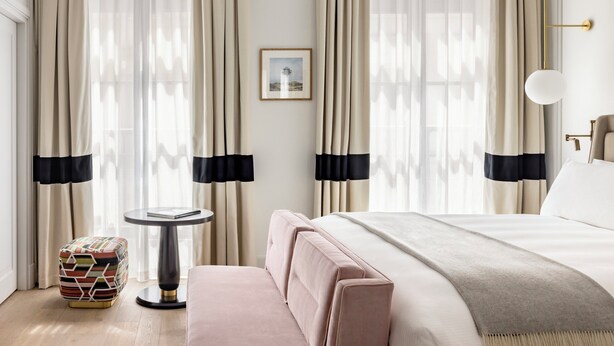 Une chambre d’hôtel avec un lit, une petite table ronde, un canapé et des rideaux.