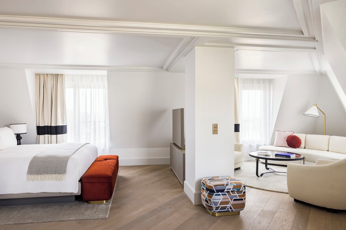 A hotel room with a bed, a sofa, a TV, a coffee table, and a small side table.