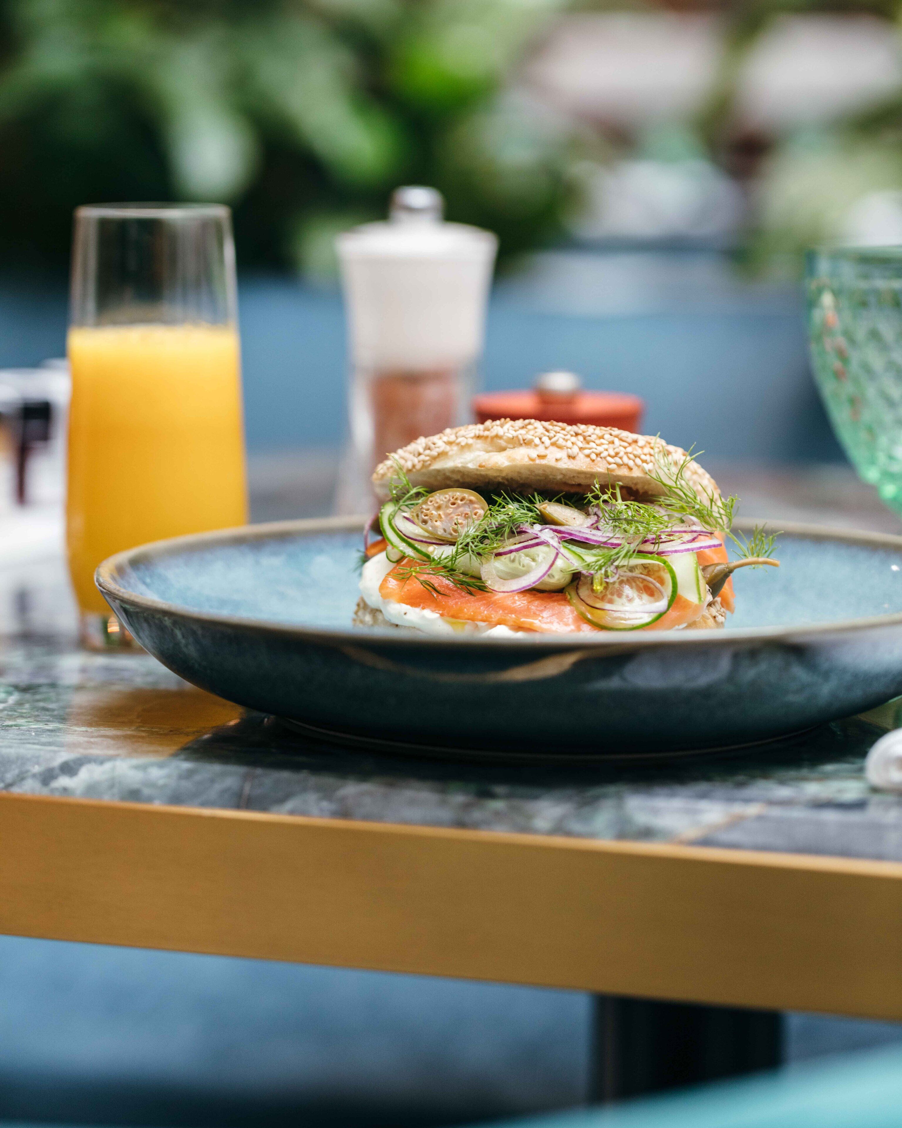 A sandwich on a plate with a glass of orange juice in the background.