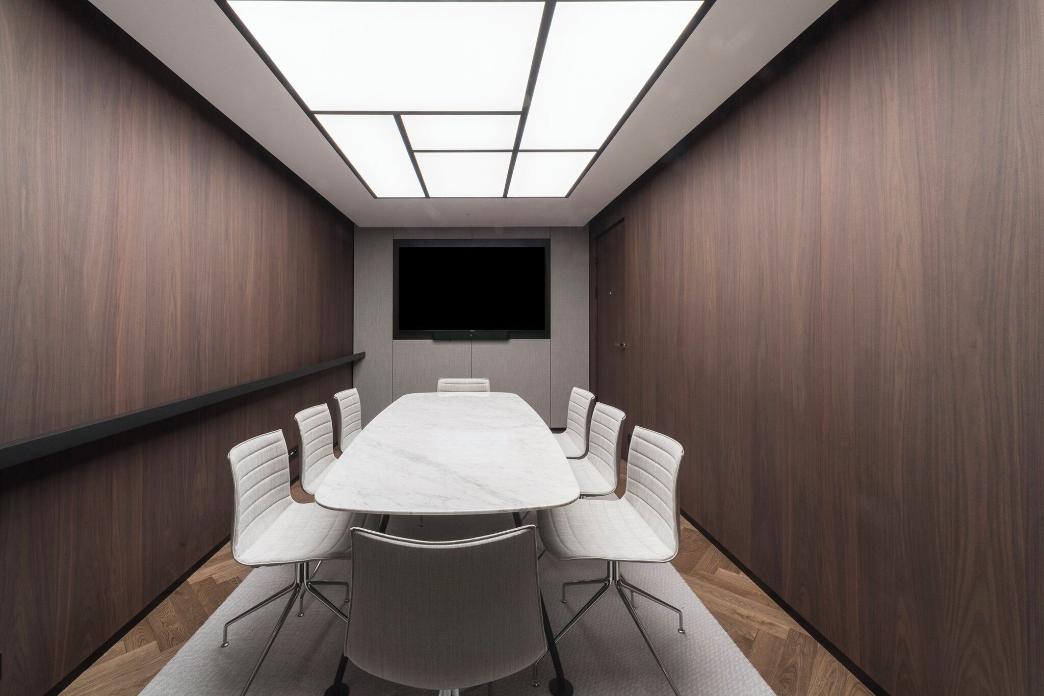 A conference room with a large table, six chairs, a flat-screen TV, and a skylight.