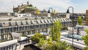 Une terrasse sur le toit, dotée d’un espace extérieur aménagé et offrant une vue sur un bâtiment historique surmonté d’un dôme verdoyant.