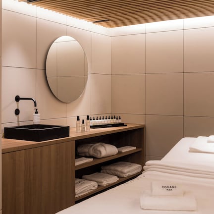 A modern bathroom with a wooden vanity, a round mirror, and neatly folded towels on the bed.