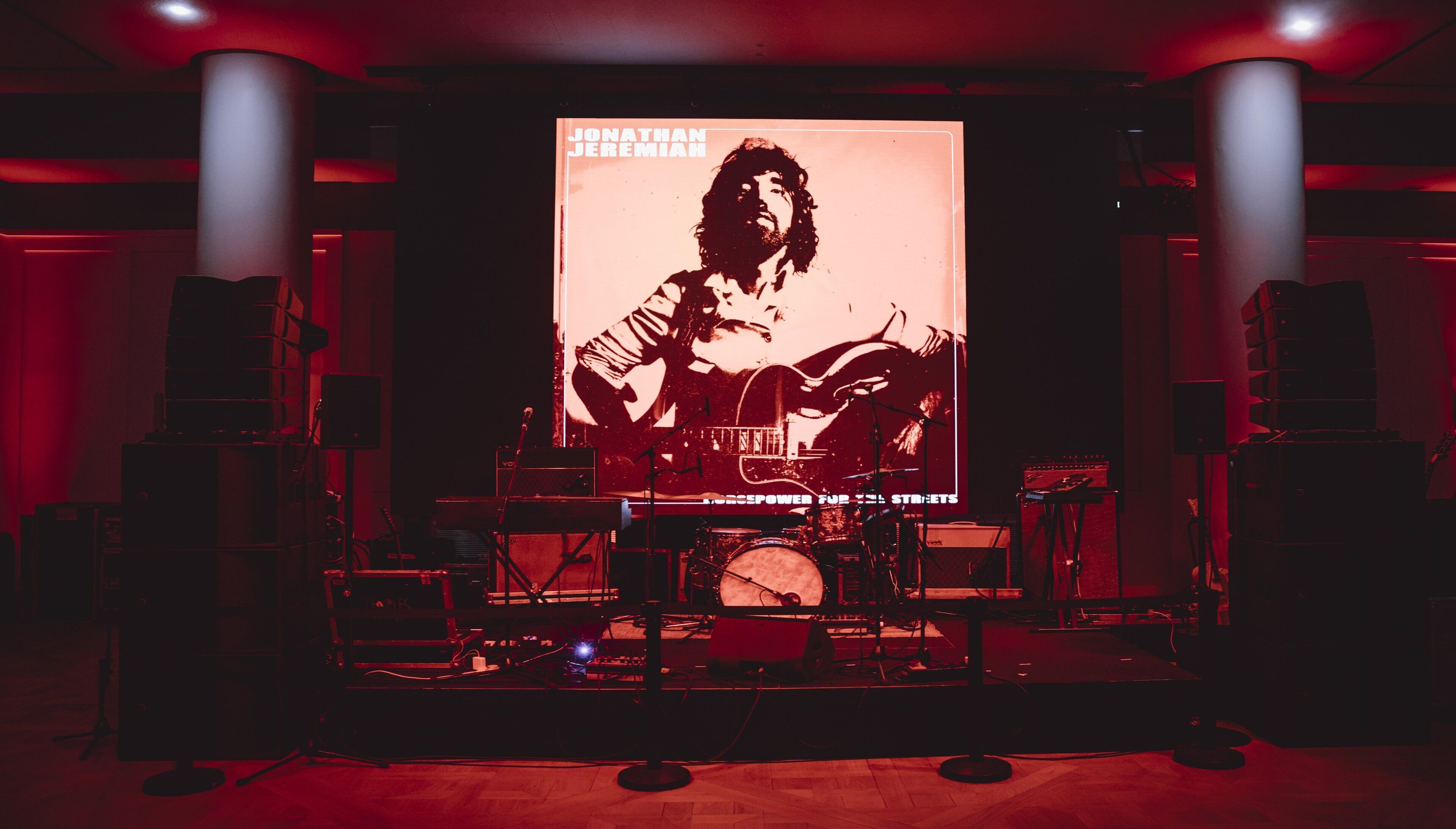A stage with musical equipment and a large poster of Jonathan Jeremiah.