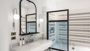 A modern bathroom with a large mirror, two sinks, a bathtub, and a glass-enclosed shower area.