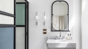 A modern bathroom with a marble sink, two wall-mounted lights, a mirror, and a door with frosted glass panels.