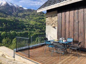 A wooden deck with outdoor furniture, a stone wall, and a mountain view.