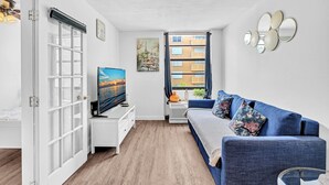 Una sala de estar moderna con un sofá azul, un televisor de pantalla plana y un ventanal con cortinas.