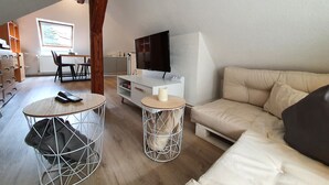 En moderne stue med sofa, fjernsyn og spiseområde med stole og bord.