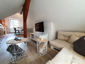 A modern living room with a sofa, a TV, and a dining area with chairs and a table.