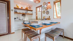 A modern kitchen with a central island, wooden stools, and decorative plates on the walls. - PF08 Ap Duplex 2 Suites - Praia do Forte (Mata de São João)