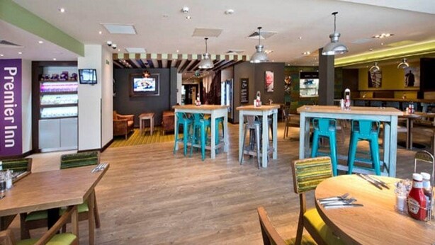 A hotel lobby with wooden flooring, multiple seating areas, and a television screen. - Premier Inn Darlington Town Centre Hotel (Darlington)