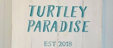 A wooden sign with 'Welcome to Turtley Paradise' and 'EST 2018' text, along with three turtle decorations.