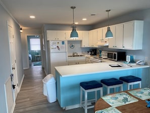 A modern kitchen with white cabinets, a central island with bar stools, a refrigerator, and a microwave.