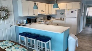 A kitchen with white cabinets, a central island with blue bar stools, a microwave, stove, and a refrigerator.