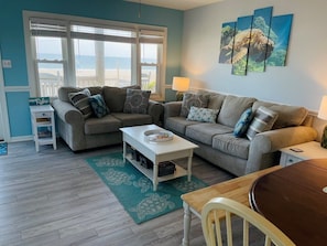 A living room with two sofas, a coffee table, a side table, a lamp, and a view of the beach. - Turtley Paradise East 3 Bedroom Home by RedAwning (Supply)