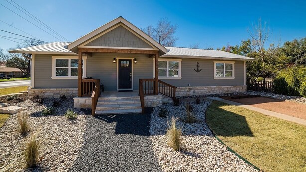 A single-story house with a front porch, a stone foundation, and a well-maintained lawn.