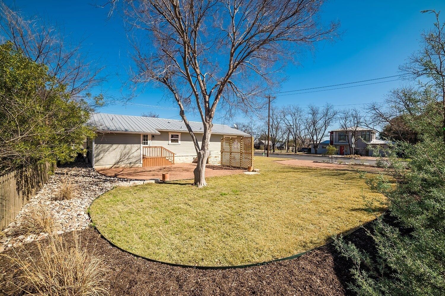 A residential property with a fenced yard, a small house with a covered porch, and a clear blue sky.