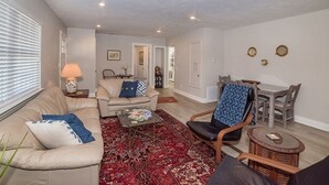 A living room with a sofa, armchair, coffee table, and a dining table with chairs.