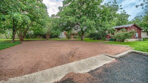 A spacious outdoor area with a gravel path, surrounded by mature trees and a red building.