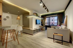 A modern living room with a sofa, a coffee table, and a TV. There is a dining area with chairs and a table. - Conforto e comodidade na Praia Iracema (Fortaleza)