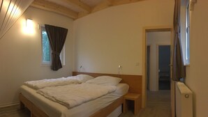 Un dormitorio con una cama de madera, una mesita de noche, una ventana con cortinas y una puerta que da a otra habitación.