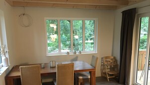 Un comedor con mesa y sillas de madera, una ventana con vistas a follaje, y una puerta que da al exterior.