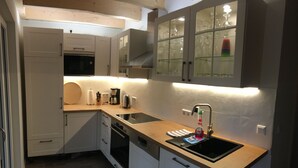 Cocina compacta con armarios blancos, estufa negra, un lavamanos y un mueble con puerta de vidrio sobre la encimera.