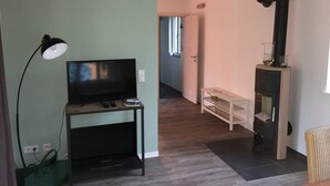 Una habitación con televisión sobre un mueble, una lámpara, una chimenea y un pasillo que conduce a otra estancia.