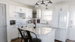 A modern kitchen with white cabinetry, a central island with bar stools, a built-in microwave, and a refrigerator. - Discover coastal charm at Holden Pattern, a spacious 4BR home in Holden Beach. (Holden Beach)