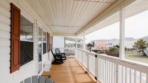 A covered porch with a wooden floor, white railings, and two chairs. - Discover coastal charm at Holden Pattern, a spacious 4BR home in Holden Beach. (Holden Beach)
