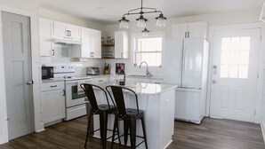 A modern kitchen with white cabinetry, a central island, bar stools, and a hanging light fixture. - Discover coastal charm at Holden Pattern, a spacious 4BR home in Holden Beach. (Holden Beach)