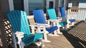 A deck with Adirondack chairs and small tables, wooden flooring, and a white railing.