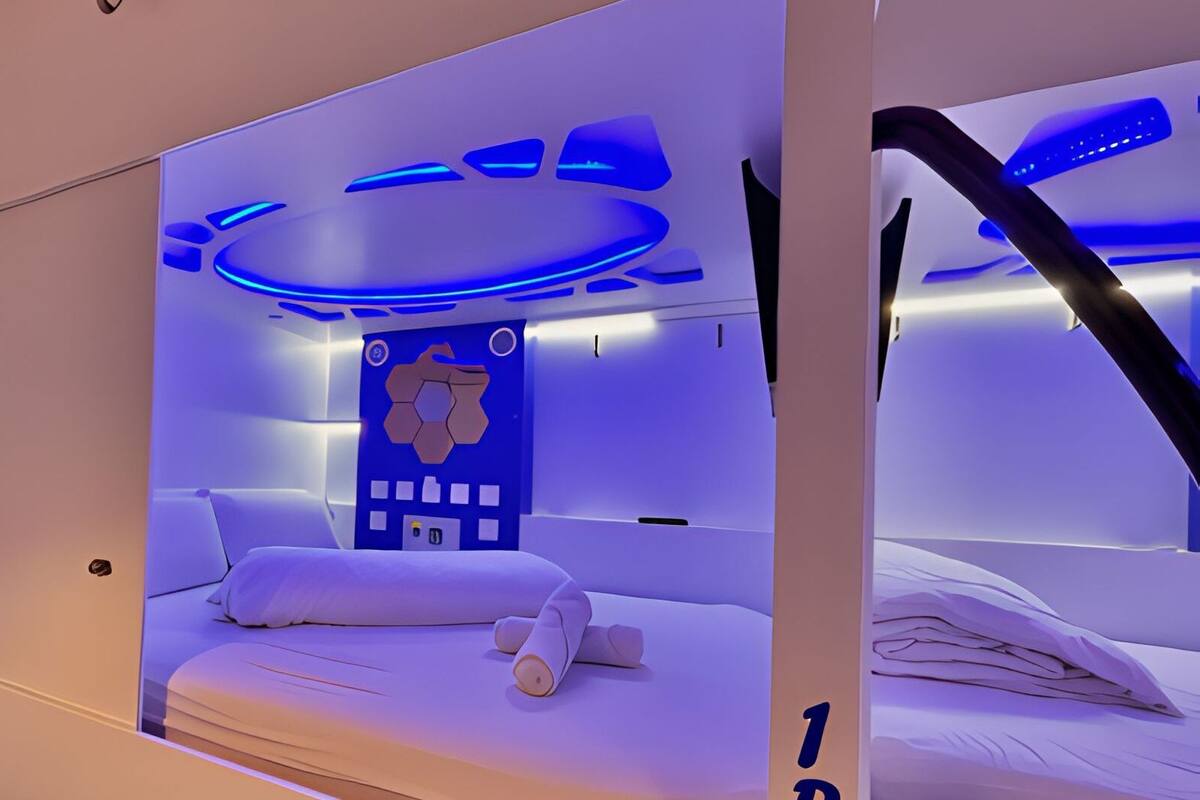A modern bedroom with a bed, a control panel, and a wall-mounted light fixture.