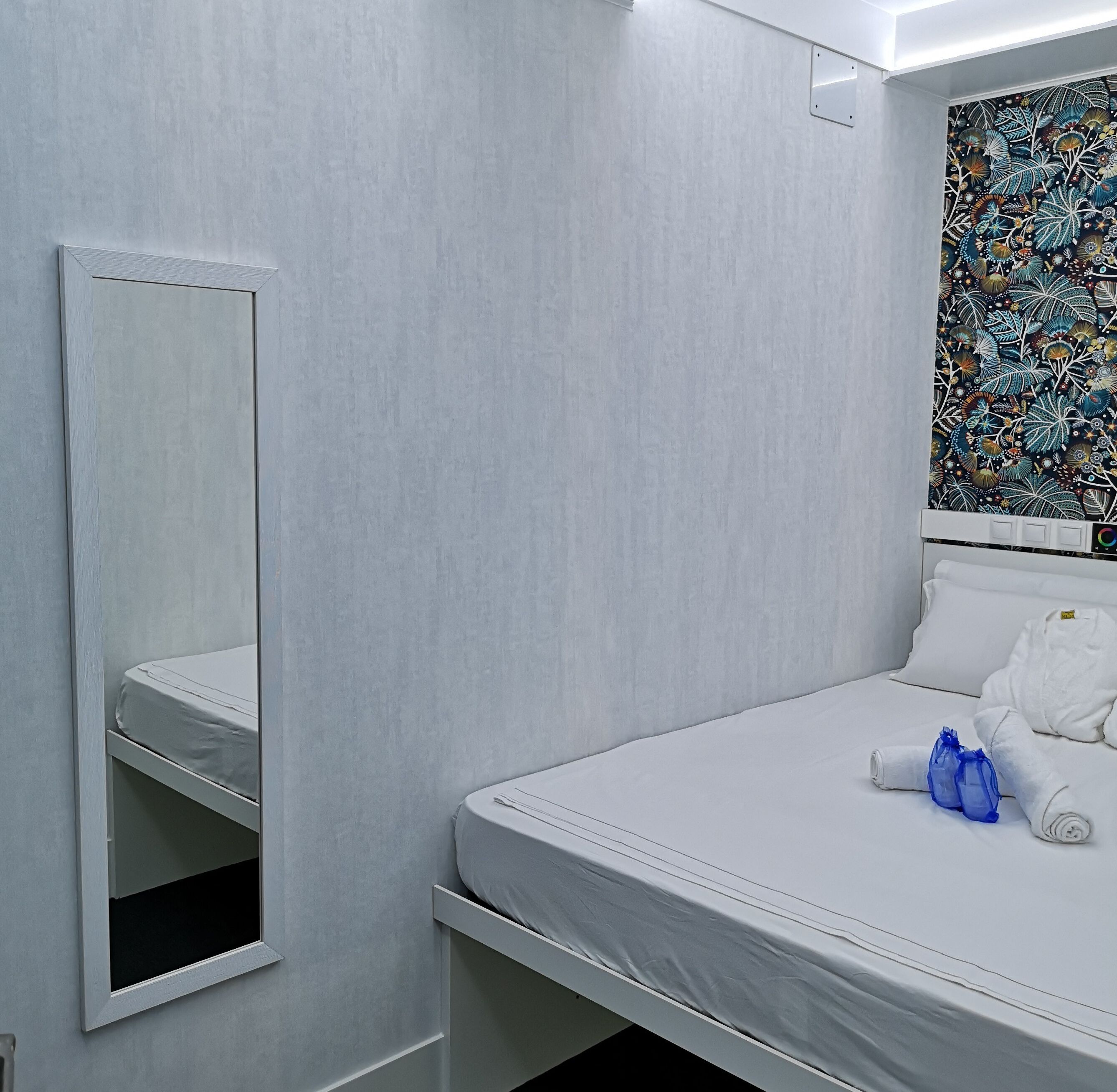 A hotel room with a bed, a large mirror, and a colorful floral wall mural.