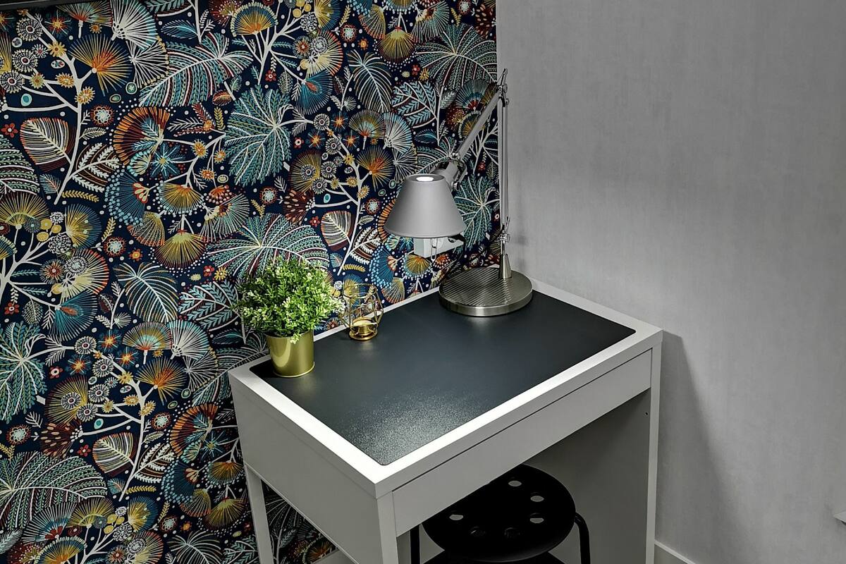 A small, modern desk with a lamp and a potted plant against a vibrant, patterned wallpaper.