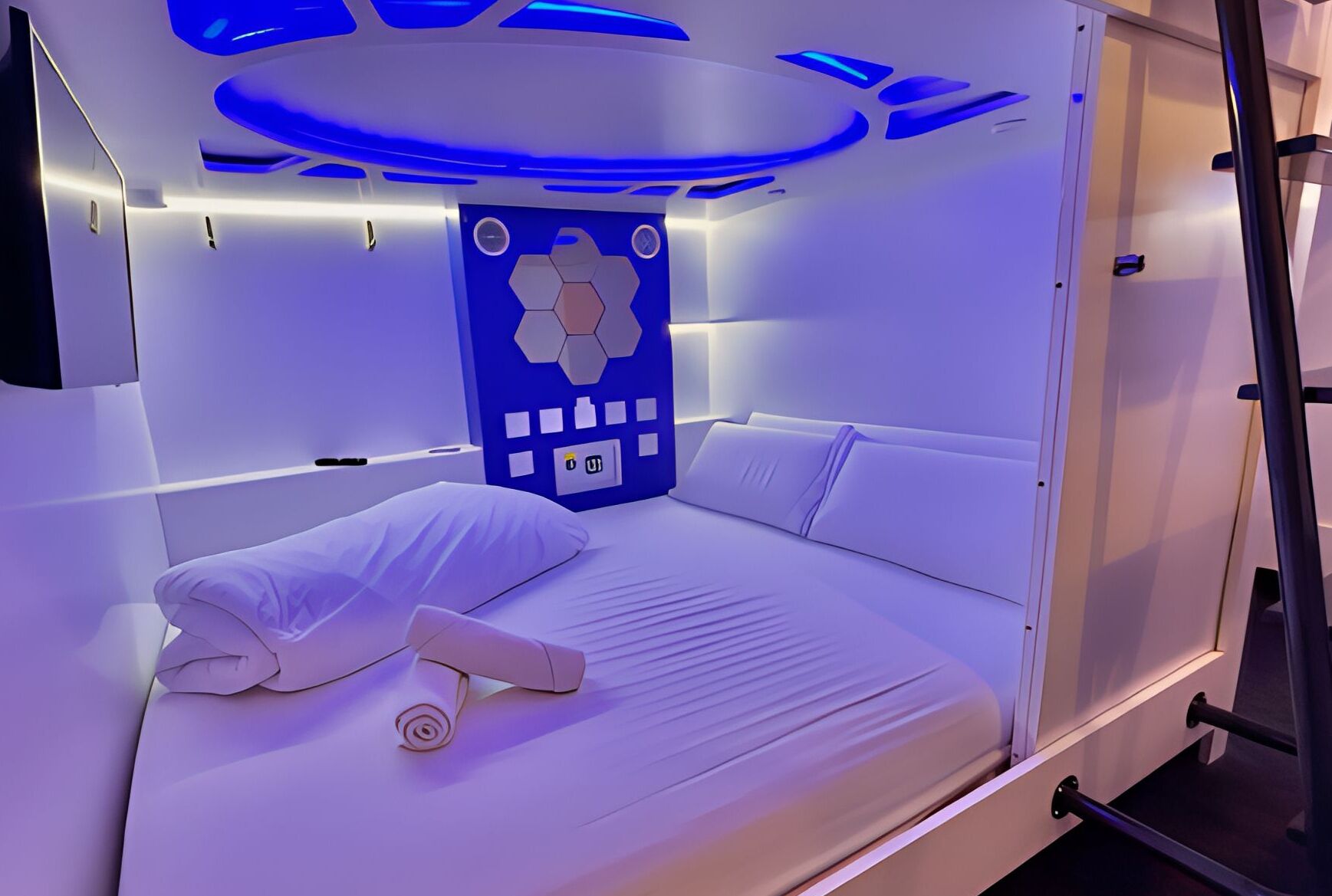 A modern, compact room with a bed, a control panel, and a unique hexagonal design on the wall.