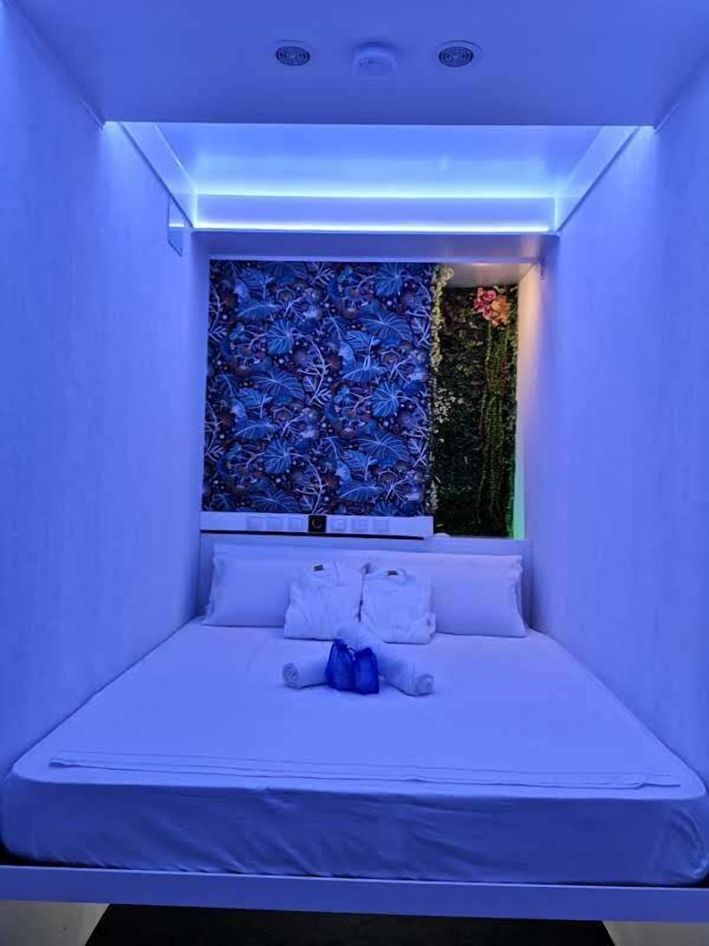 Een kleine, moderne kamer met een bed, een raam met decoratieve wand en een plafondlamp.