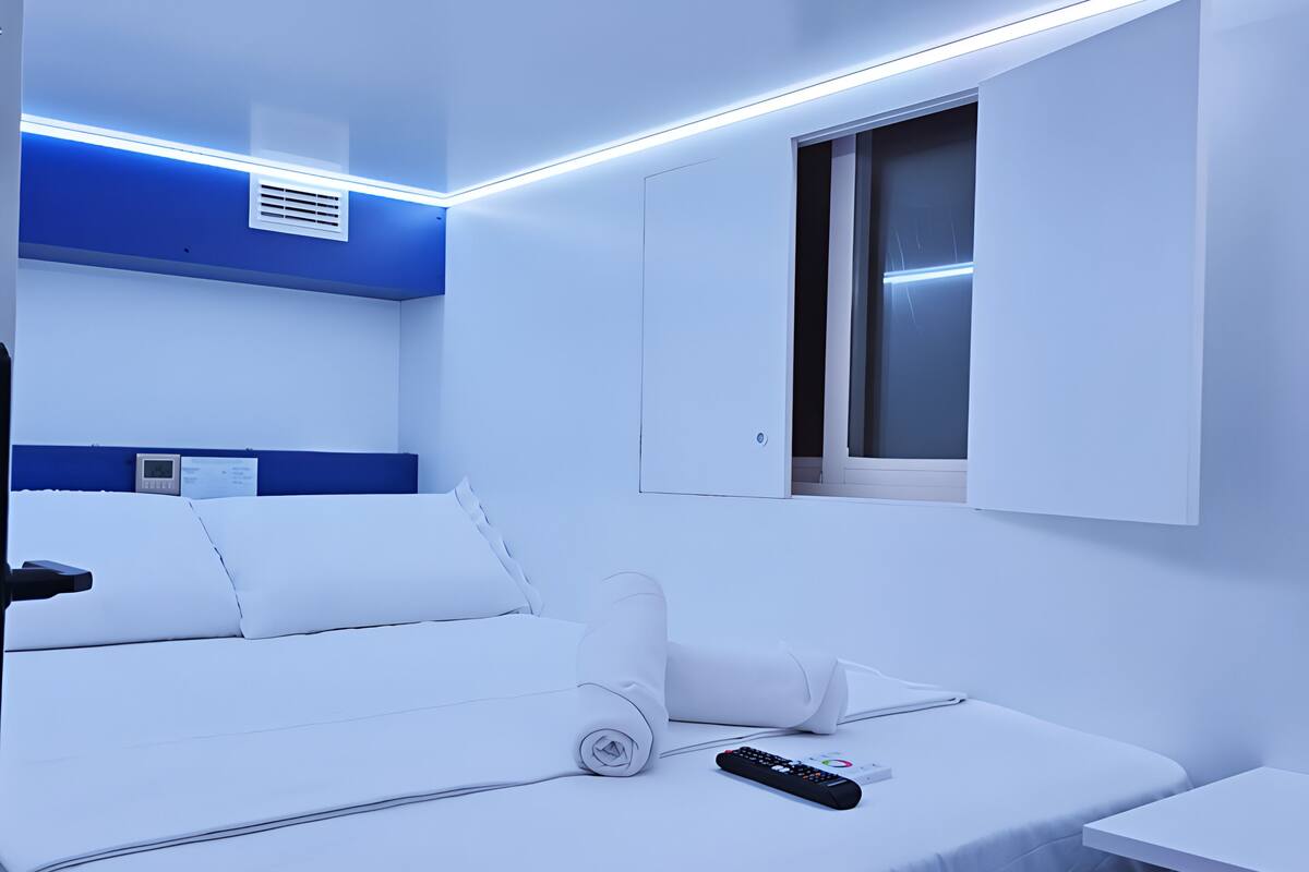 A modern hotel room with a neatly made bed, a remote control, and a window with blinds.