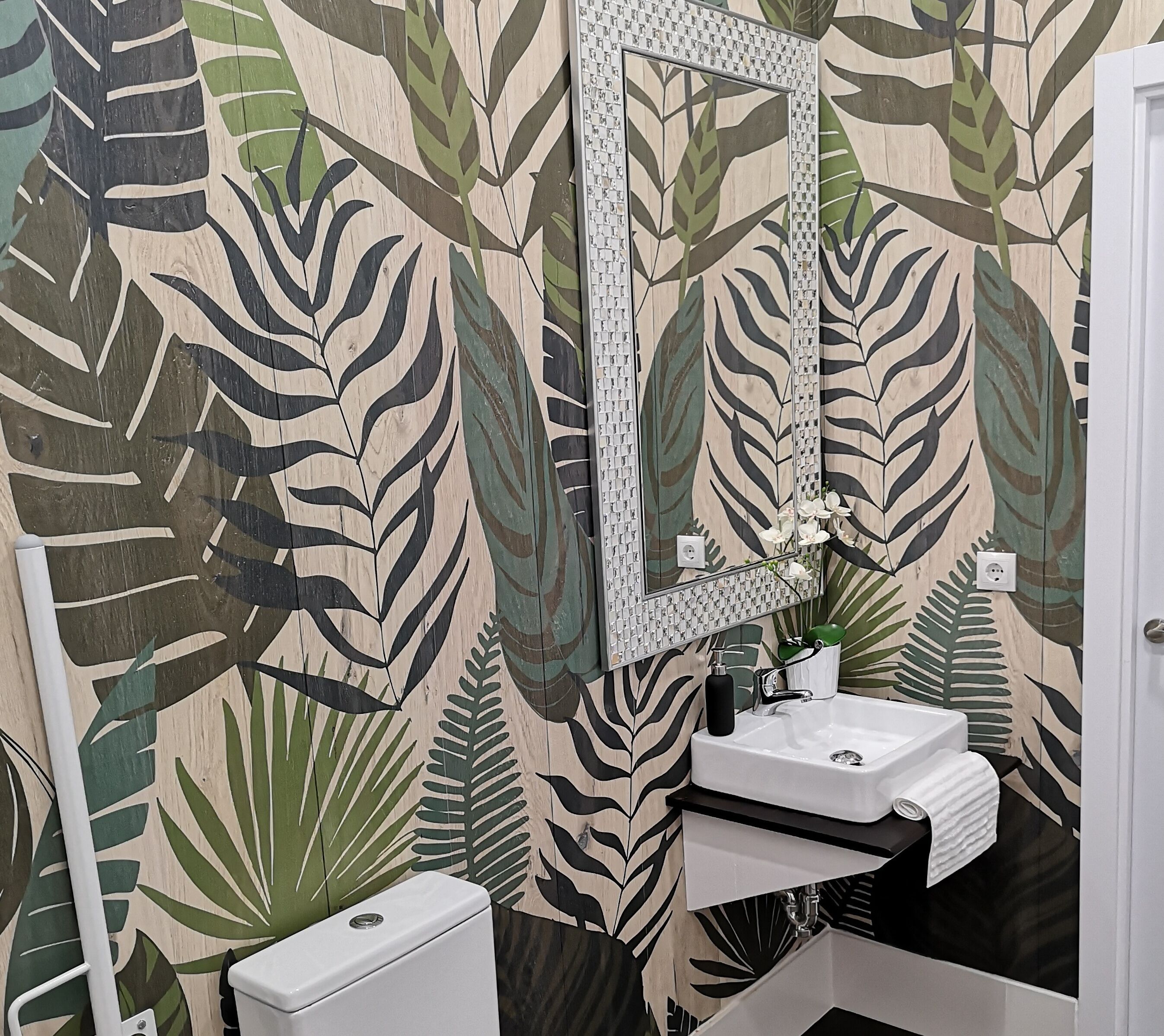 Een badkamer met toilet, wastafel en spiegel. De wanden zijn versierd met een bladmotief.
