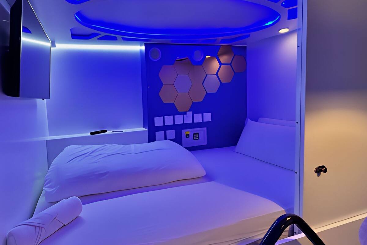 A modern, minimalist room with a single bed, a control panel, and a unique hexagonal wall design.