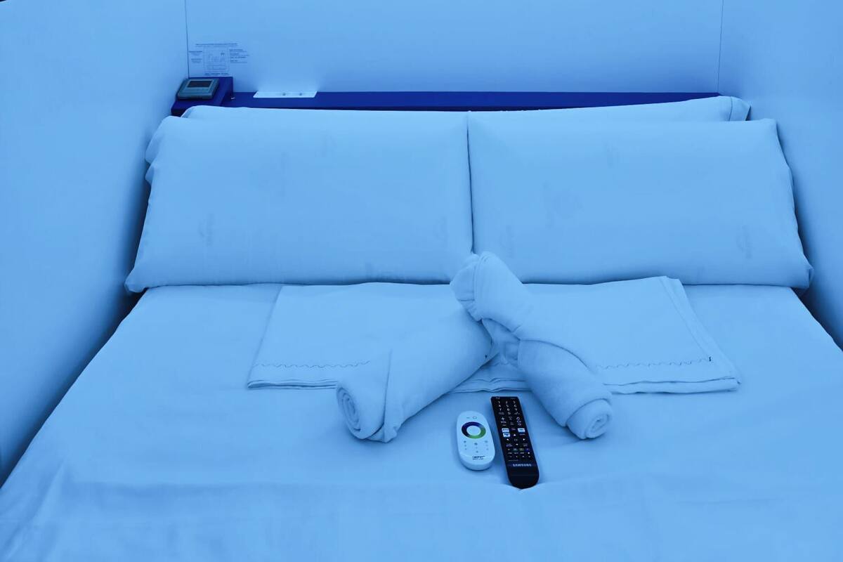 A neatly made bed with white linens, a remote control, and a digital device on the side.